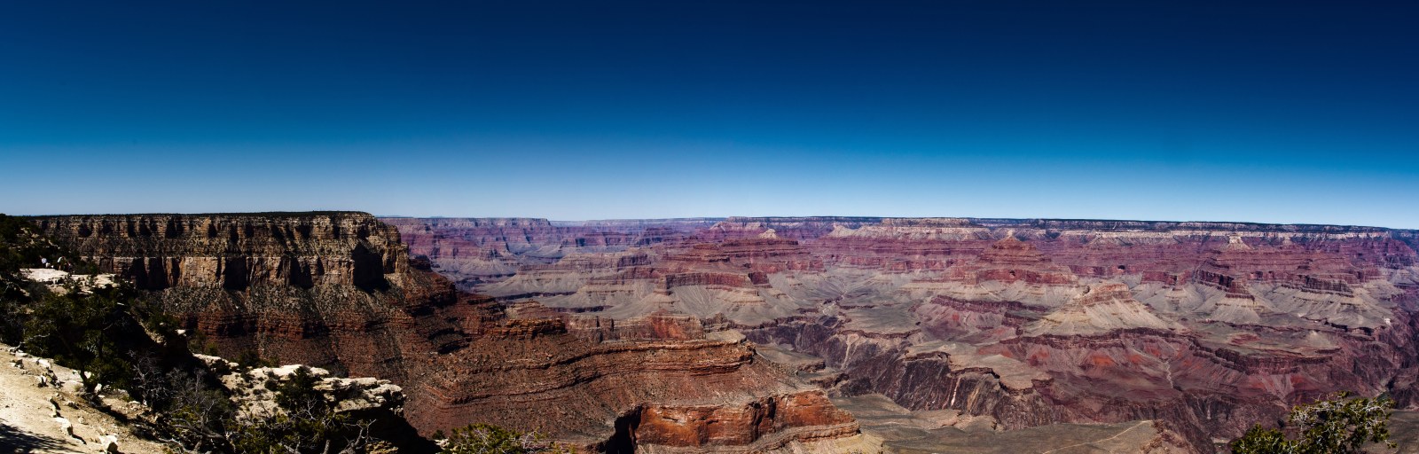 Wide view over the layered red cliffs of the Grand Canyon under a deep blue sky, with snow along the rim