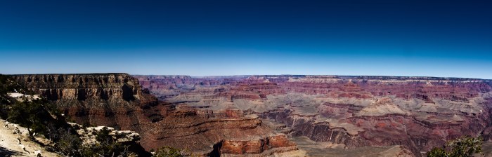 Wide view over the layered red cliffs of the Grand Canyon under a deep blue sky, with snow along the rim