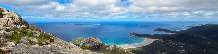 Turquoise bay with a curved white beach seen from a rocky summit, small islands on the horizon