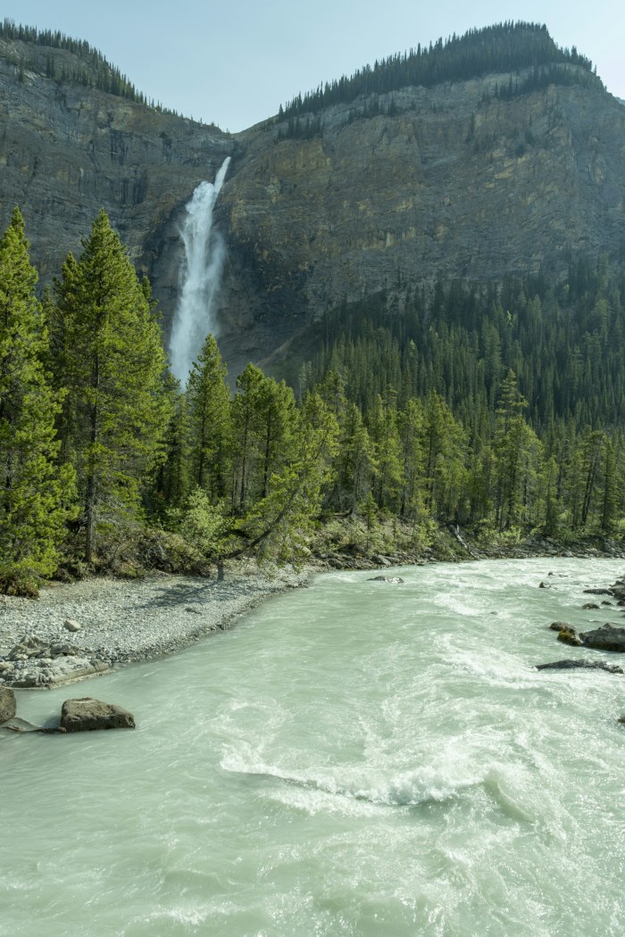 Waterfall cascades down a rocky cliff into a river — Waterfalls wallpaper