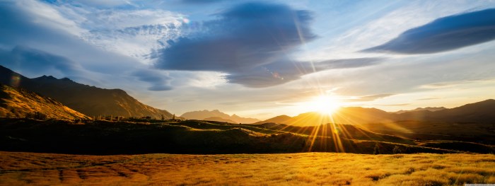 Golden grass fields and mountains near Queenstown, New Zealand, with the sun setting behind the hills