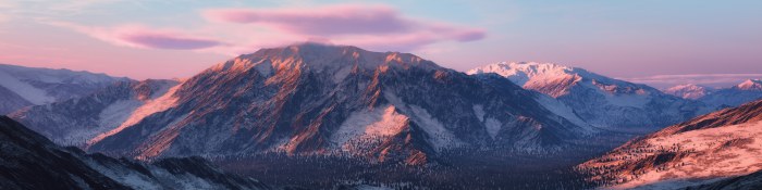Snow-dusted mountain range glowing pink at sunset beneath soft lenticular clouds